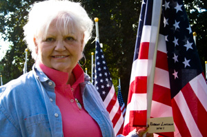 Elderly woman standing next to flag.